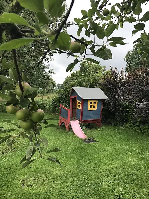 Een appelboom met appels, en daarachter het speelhuisje met glijbaan