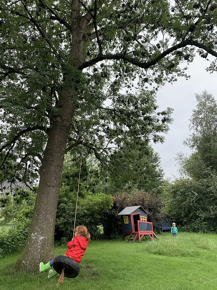 Een kind op de bandschommel onder de grote boom in de tuin van De Tuin van Meta